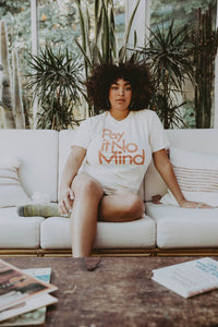 Woman sat on a white sofa wearing White Pay It No Mind Shirt in Unisex by The Bee and The Fox