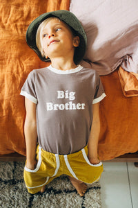 Kid lying on the edge of a bed wearing Big Brother Ringer Tee for Kids by The Bee and The Fox