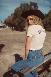Woman sits on gate and cowboy hat in Cream Bull Shirt for Women by The Bee and The Fox