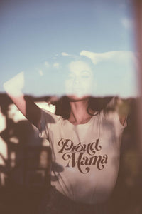 Woman in a window wearing Proud Mama Scoop Neck Shirt for Women by The Bee and The Fox