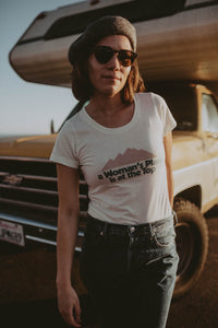 Woman stood in front of a camper wearing A Woman's Place is at the Top Scoop Neck Shirt by The Bee and The Fox