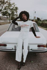 Woman leaning on a car wearing White Always Give a Damn Shirt in Unisex by The Bee and The Fox