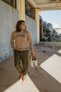 Man on a beach wearing Unisex Tan Do No Harm + But Take No Shit crewneck by The Bee and The Fox