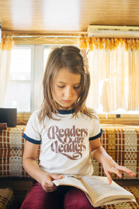 Little girl reading wearing Readers Are Leaders Shirt for Kids by The Bee and The Fox