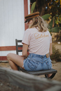 Woman sat backwards on a chair wearing Peach Women for Women Sisterhood Shirt by The Bee and The Fox